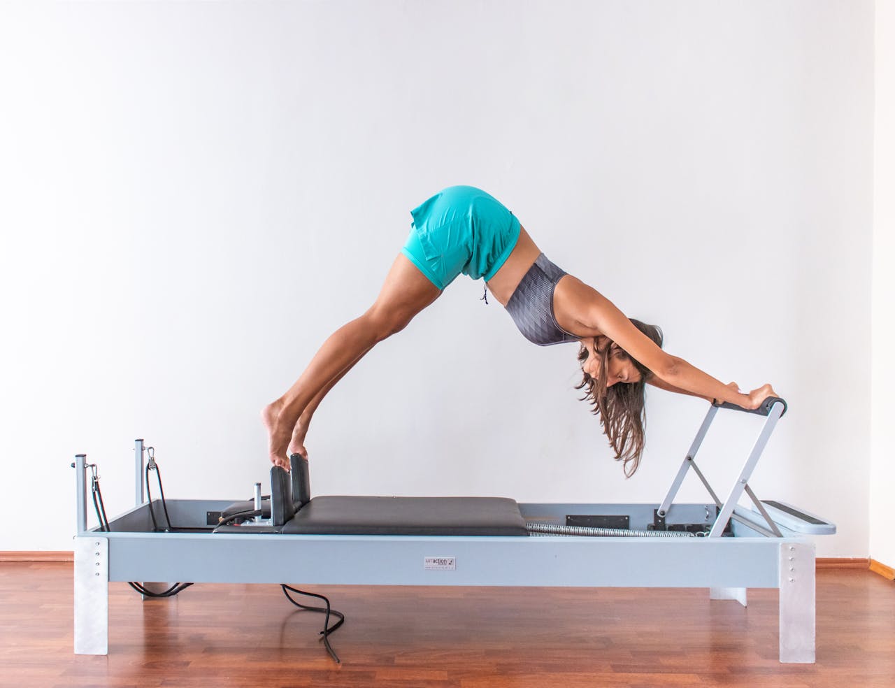 services-02 A woman performs a pilates exercise on a reformer, demonstrating flexibility and fitness indoors.